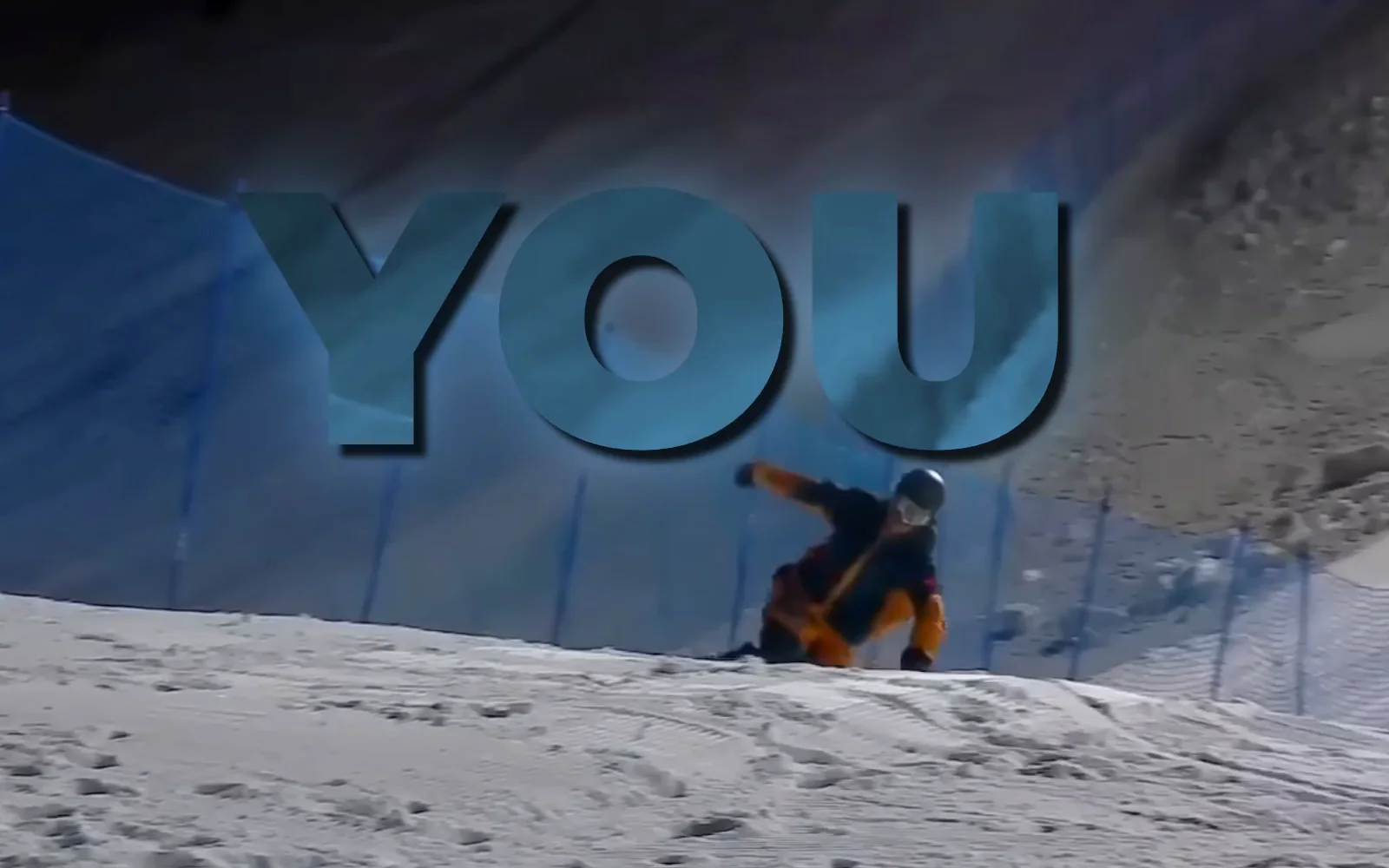 A frame from the snowboard edit: the lyric “YOU” in large blue glass letters, with the rider cut out in front of it, his helmet over the U